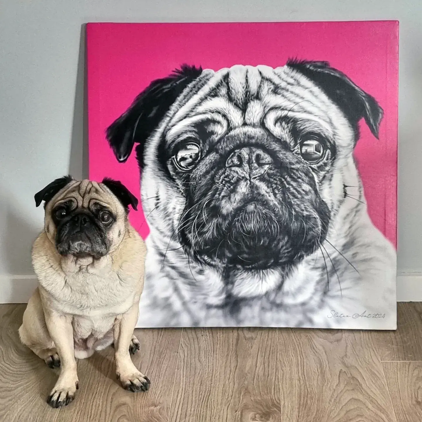 A pug sitting beside a large canvas print of its digital portrait